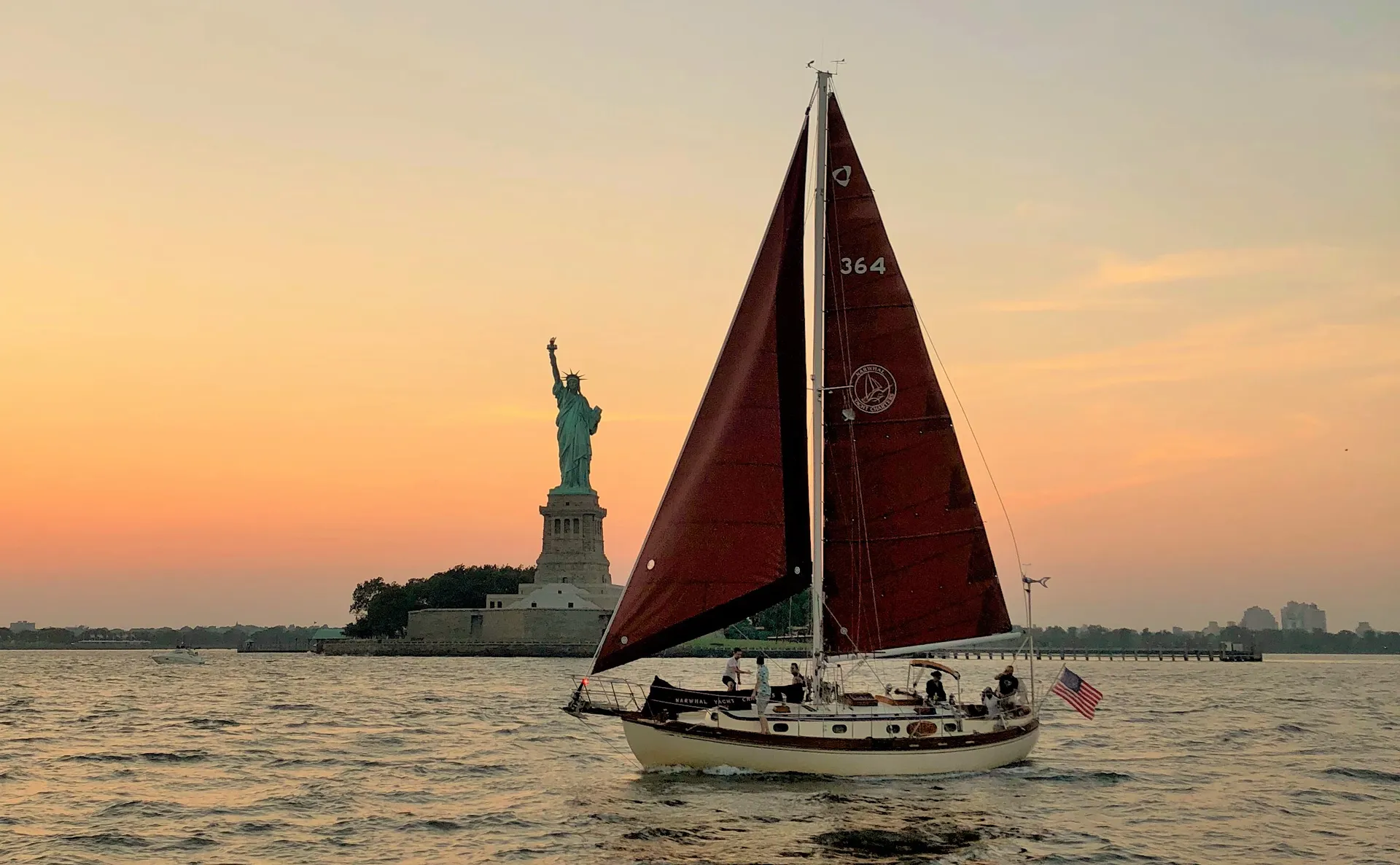 Classic sailboat passing the Statue of Liberty at sunset